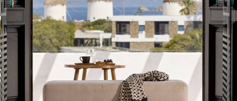 A balcony with a sofa, a small table, and a view of windmills and a building.