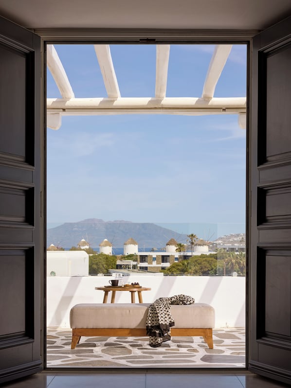 A balcony with a sofa and a table, a view of windmills, and a mountainous landscape.