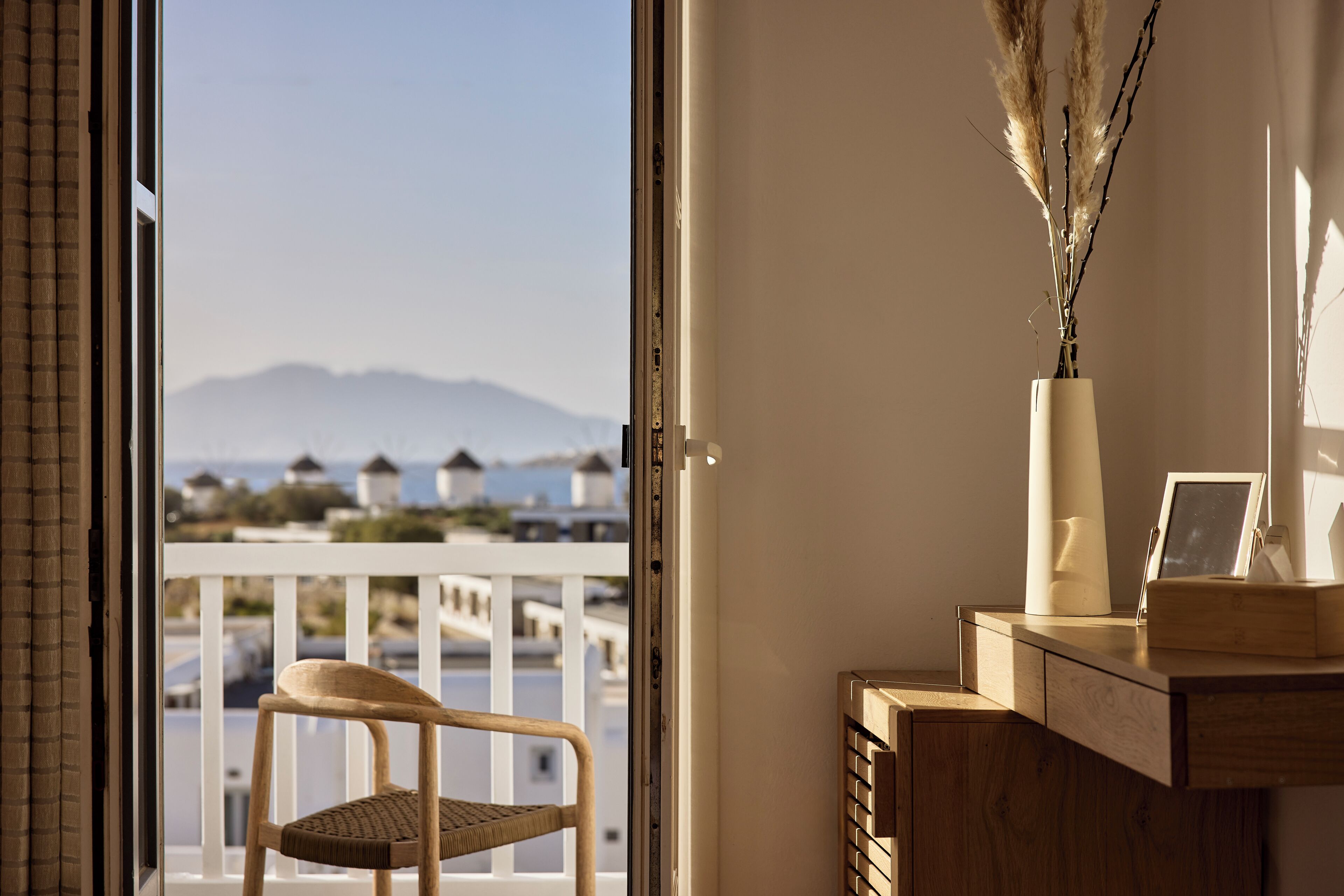 A balcony with a wicker chair, a vase with pampas grass, and a wooden desk with a picture frame.