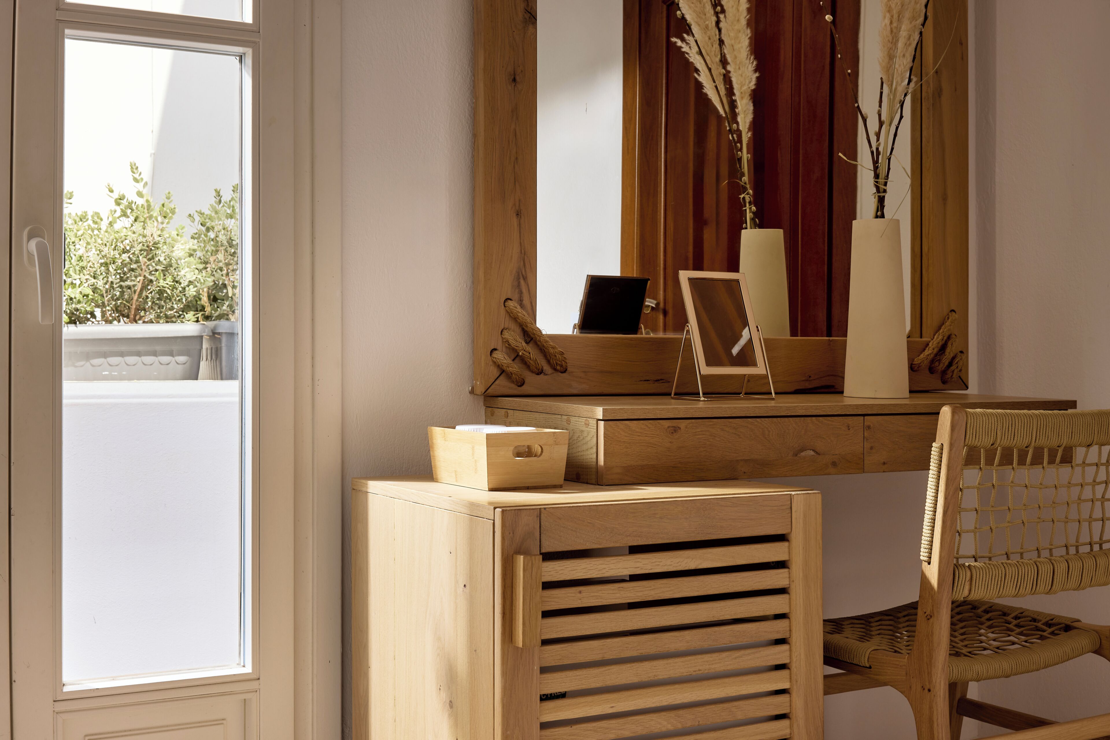 A wooden desk with a laptop, a vase with dried plants, and a wicker chair.