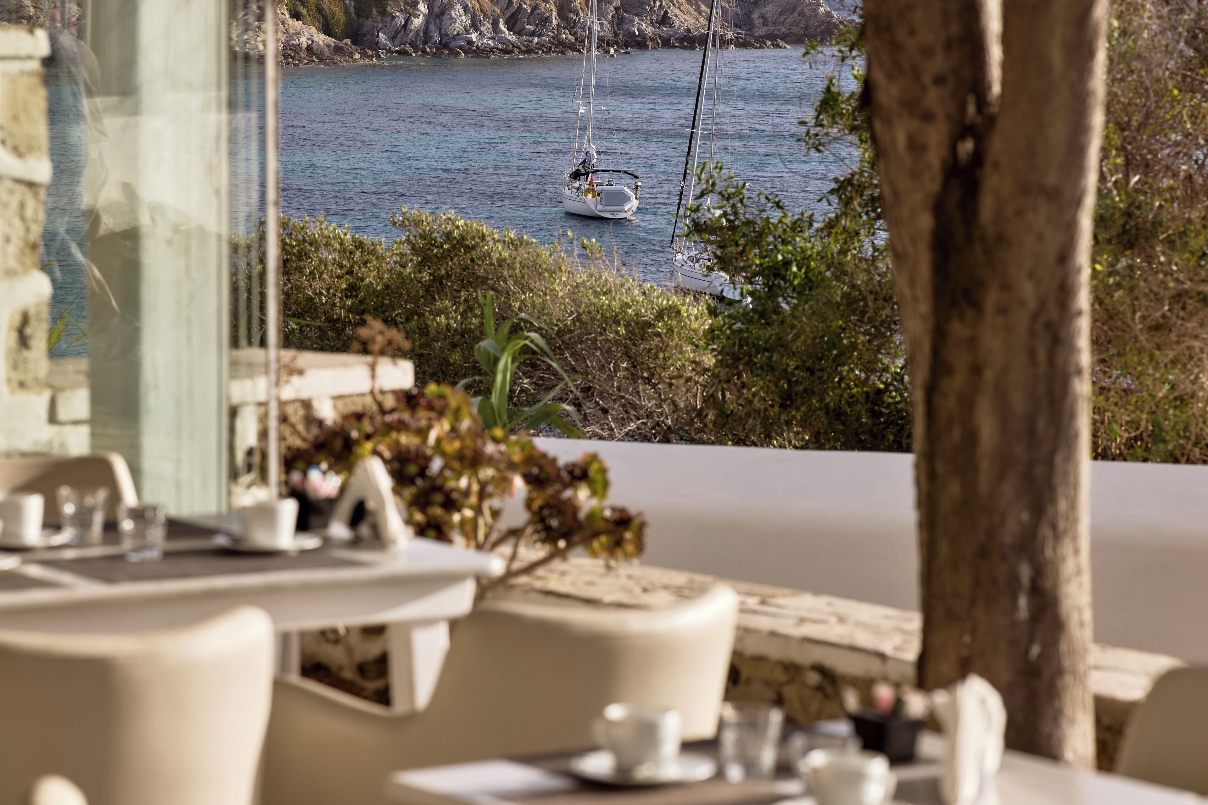 A seaside dining area with tables and chairs, a view of the sea, and a rocky coastline.