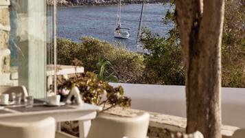 A seaside dining area with tables and chairs, a view of the sea, and a rocky coastline.