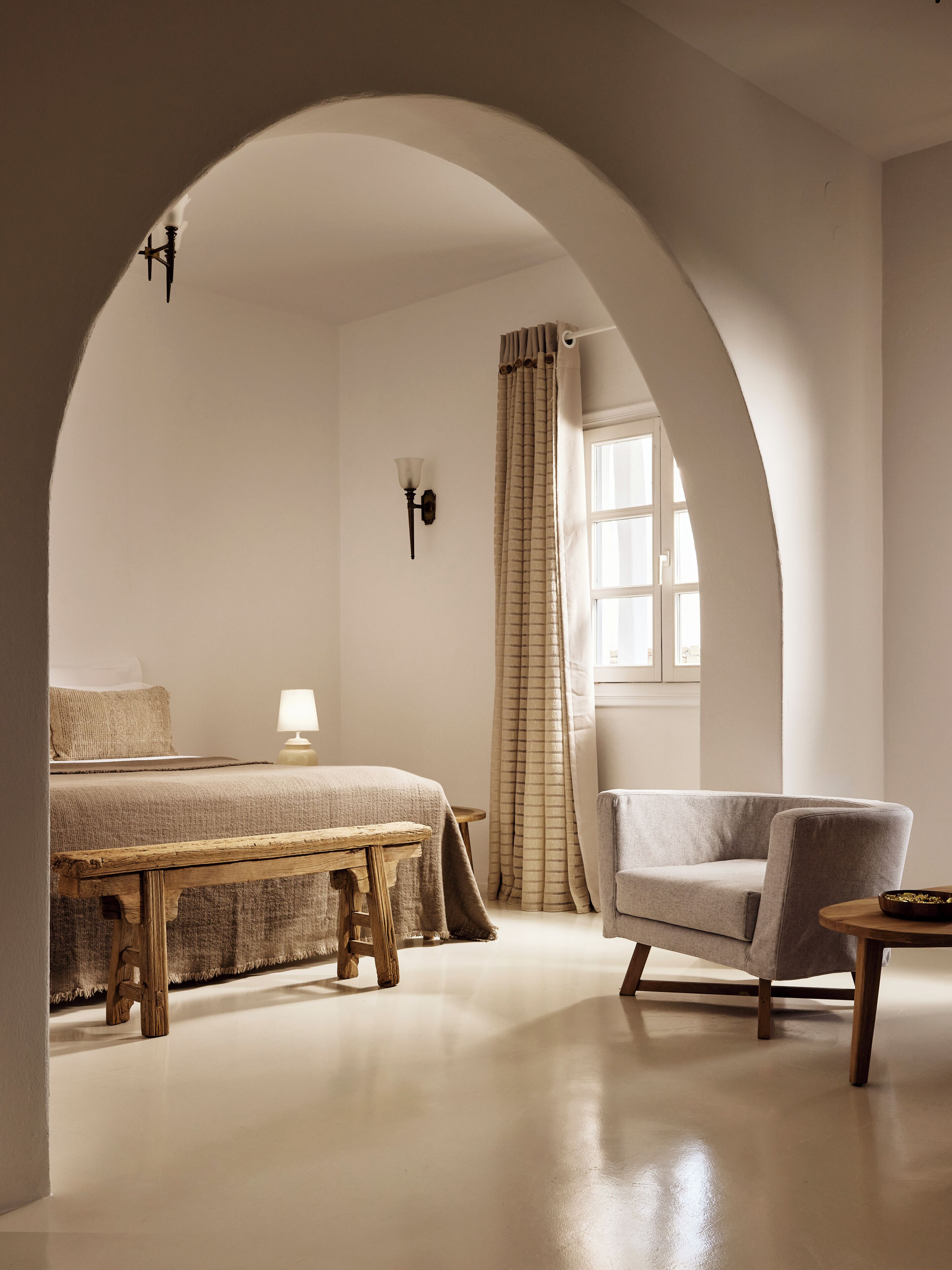 Un dormitorio con cama, mesita de noche, lámpara, silla y ventana con cortinas.