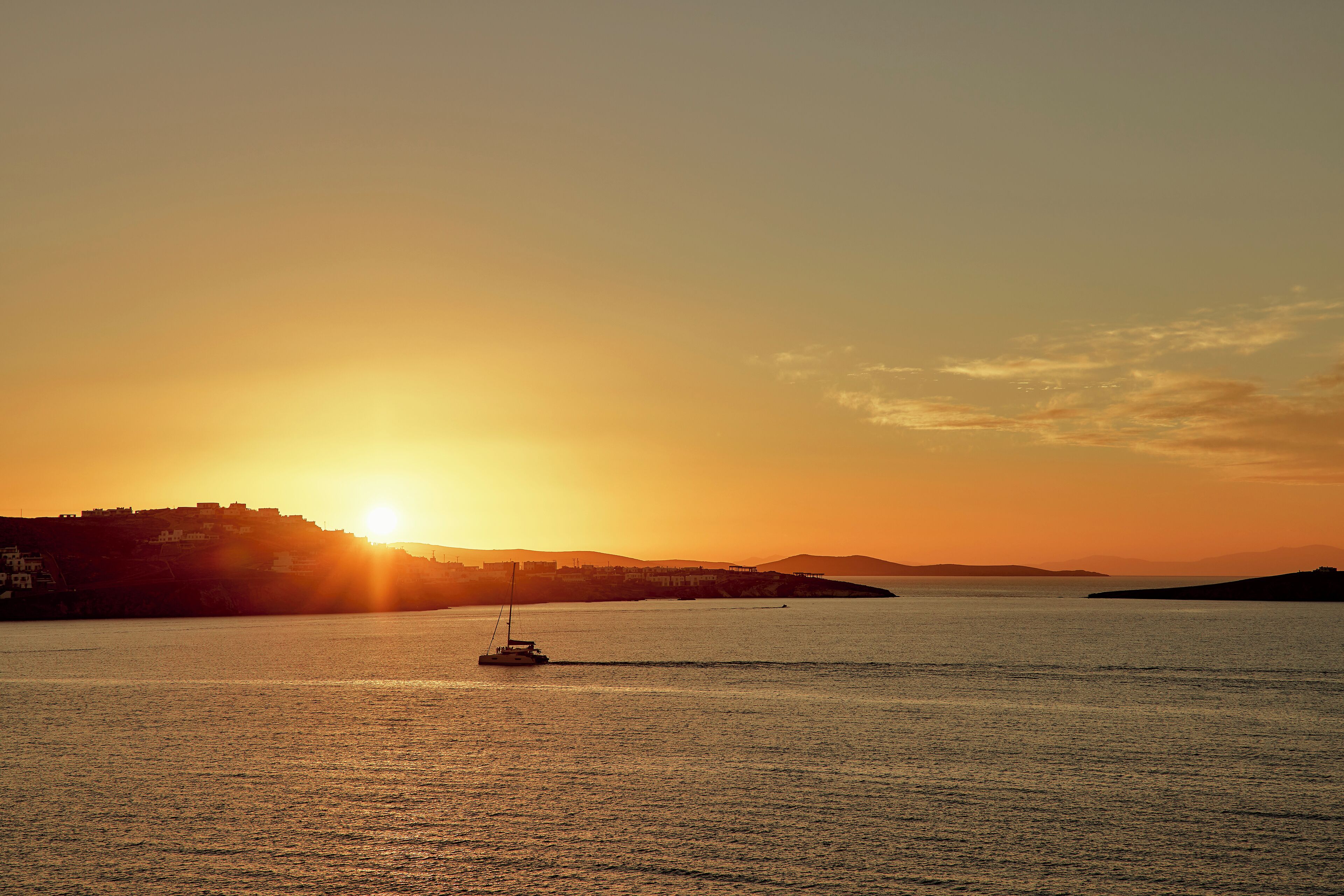Un atardecer sobre un mar en calma con un velero.