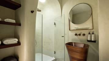 Un baño con ducha de vidrio, lavamanos de madera y repisas con toallas dobladas.