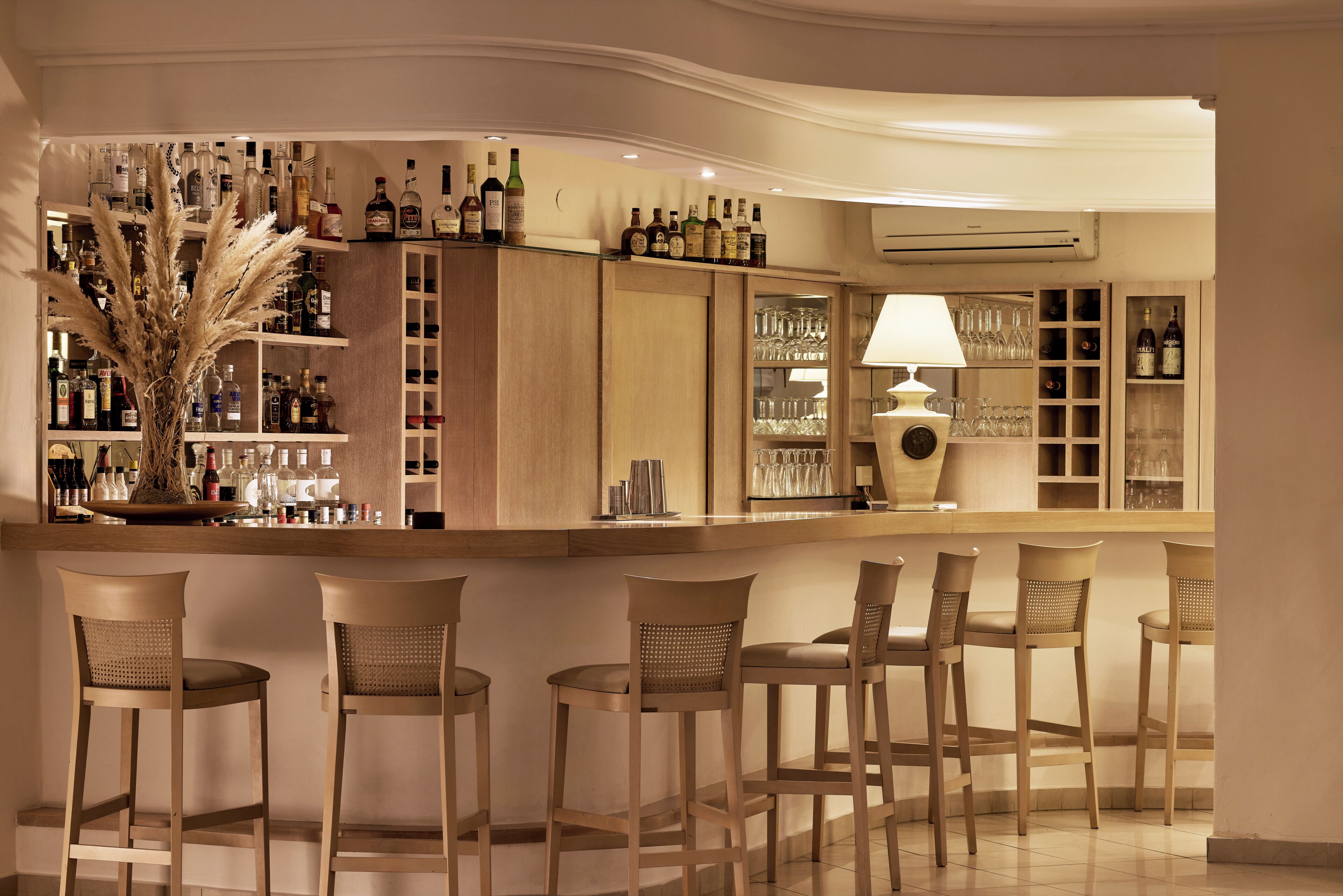 Una zona de bar con sillas de madera, estantes llenos de botellas de licores y un jarrón decorativo.