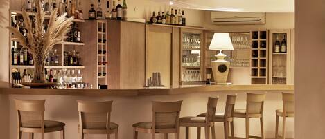 Una zona de bar con sillas de madera, estantes llenos de botellas de licores y un jarrón decorativo.