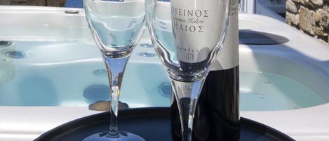 A bottle of wine and two glasses on a table with a hot tub and a scenic view of the sea and buildings in the background.