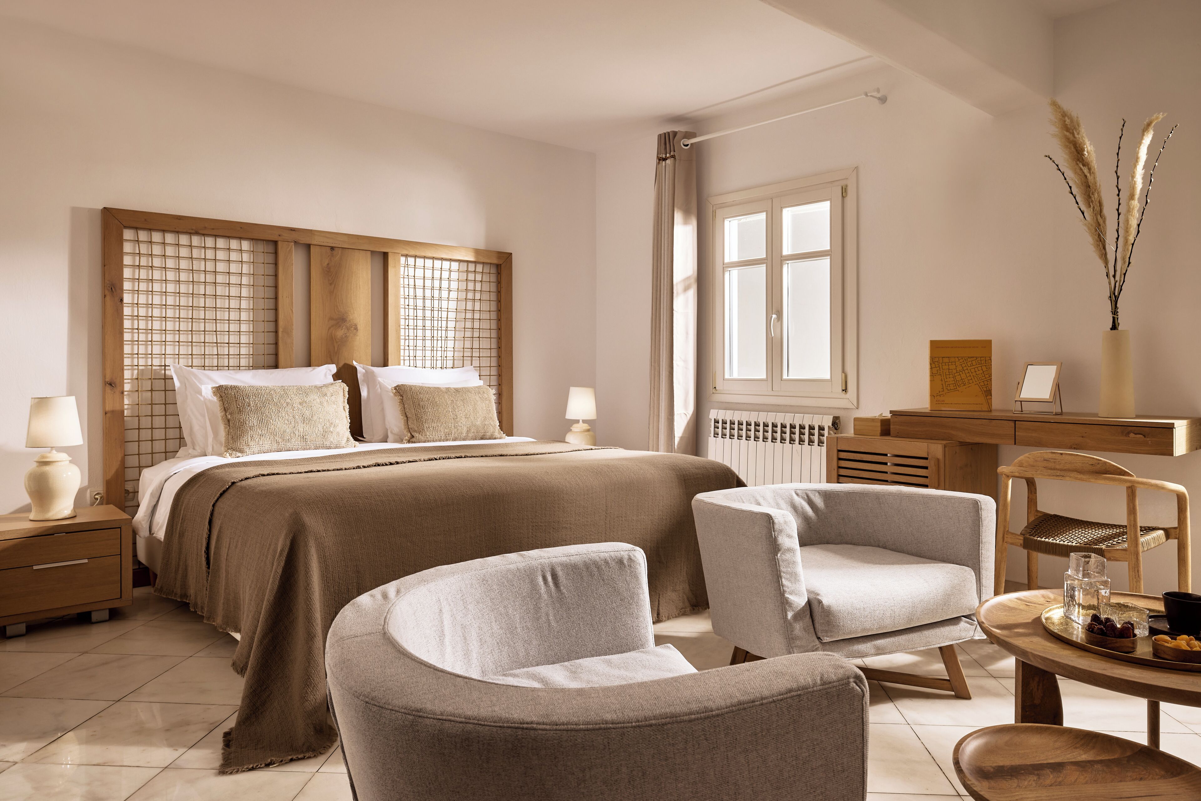 Een slaapkamer met een groot bed, twee nachtkastjes, een bureau, een stoel en een raam met gordijnen.