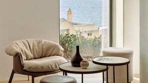 Una sala de estar moderna con un sillón color beige, una mesa redonda con un florero y un pequeño reposapiés.