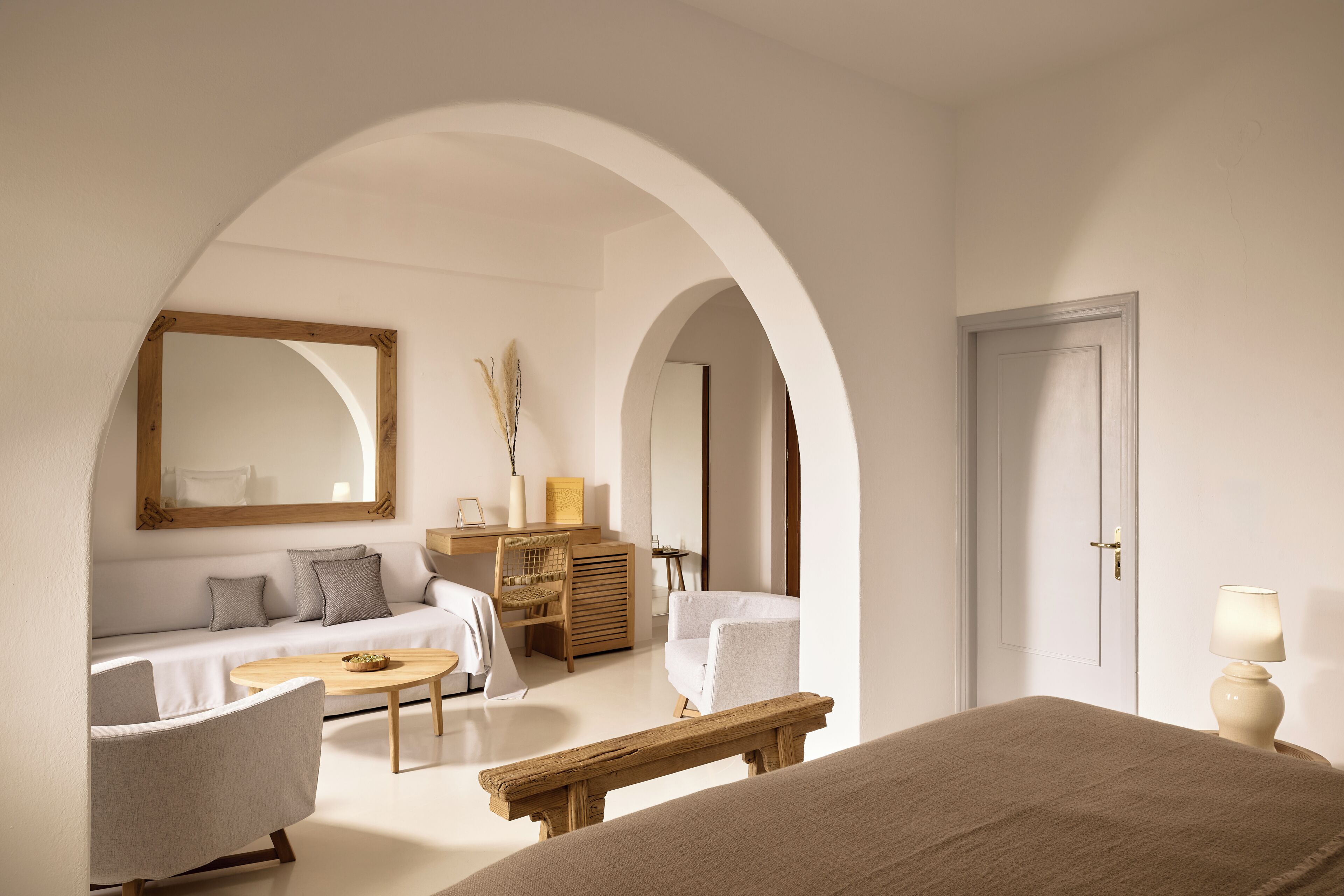 Una habitación con cama, sofá, banca de madera, escritorio y lámpara.