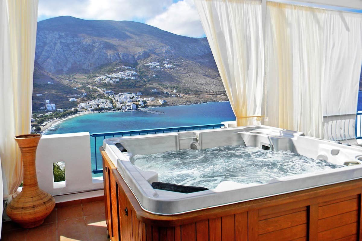 A hot tub on a balcony with a view of a coastal town and mountains.