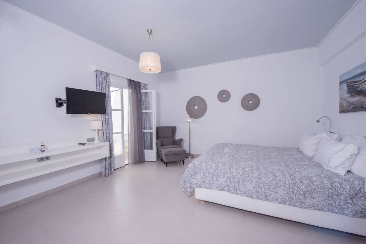 A bedroom with a bed, a TV, a chair, a desk, and a window with curtains.