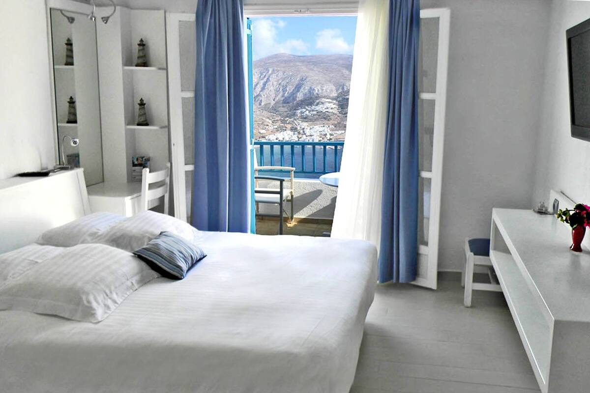 A bedroom with a large bed, a desk, and a view of a mountainous landscape.