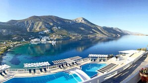 Una piscina di un resort con acqua cristallina, circondata da edifici bianchi e con una montagna sullo sfondo.