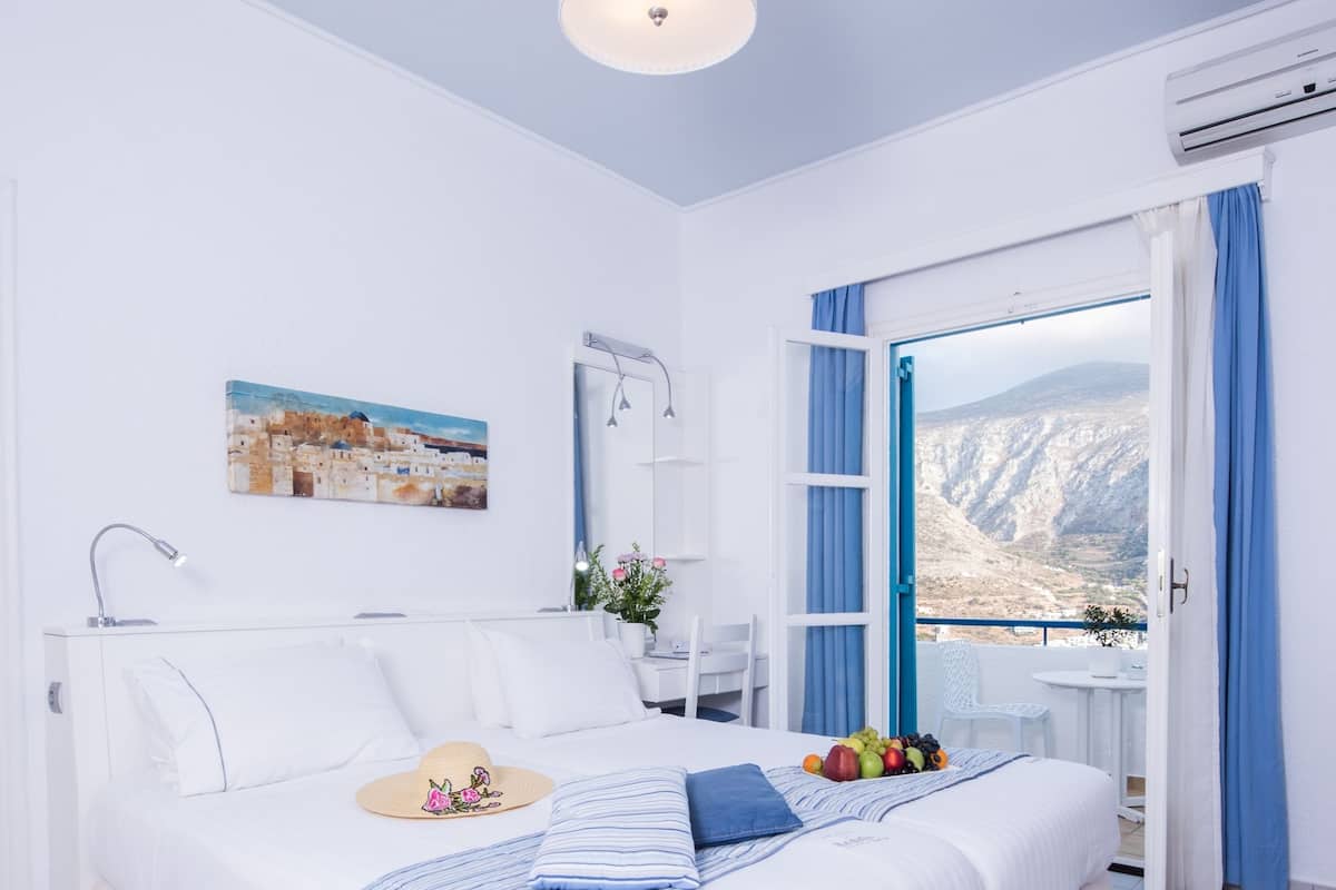 A spacious bedroom with a large bed, a bedside table, a window with a view of the landscape, and a ceiling light.