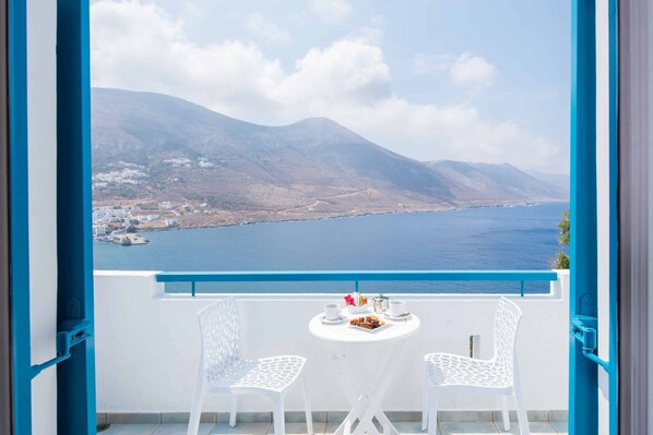 A balcony with two white chairs and a small table set for two, overlooking a coastal landscape with mountains and a body of water. - Aegialis Hotel & Spa (Amorgos)