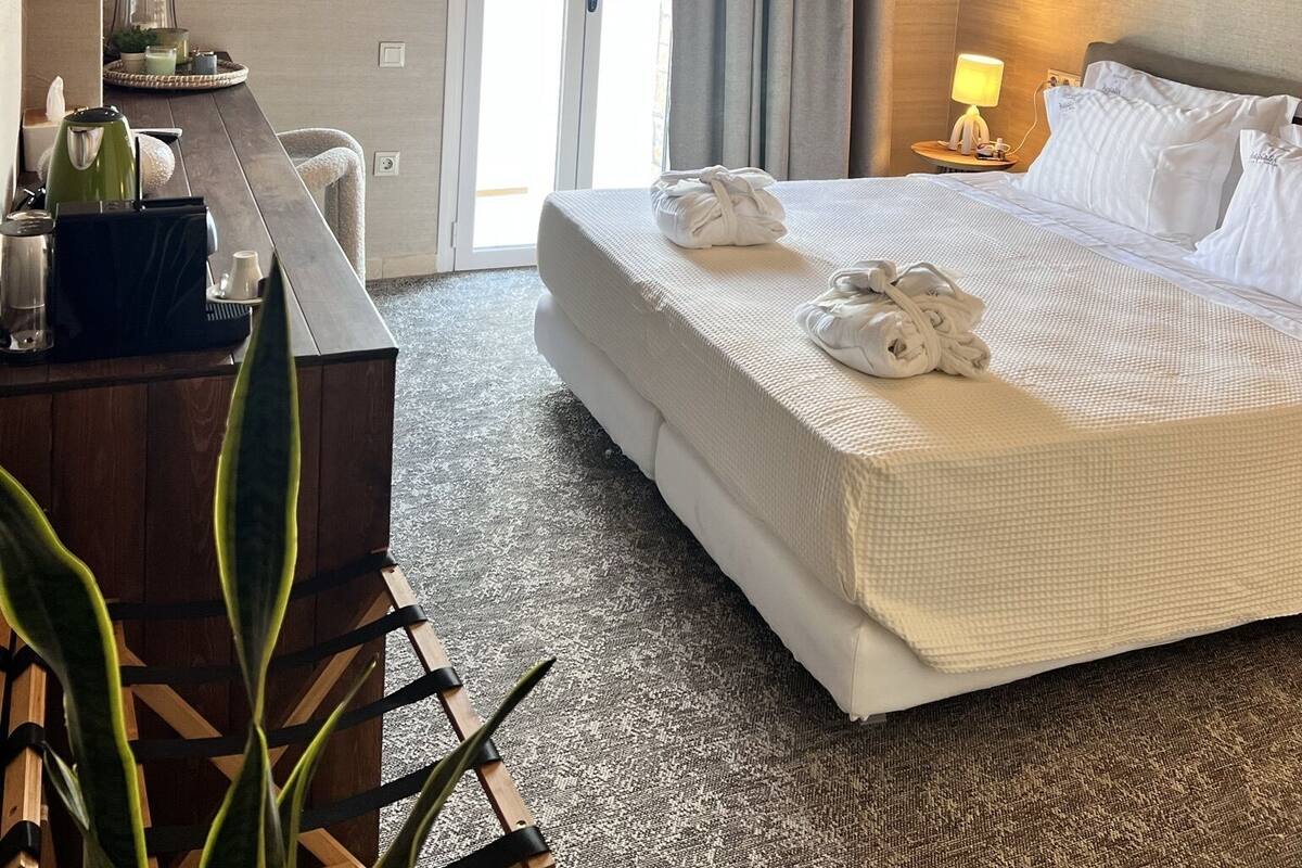 A hotel room with a large bed, a desk with a kettle, a lamp, and a hanging light fixture.