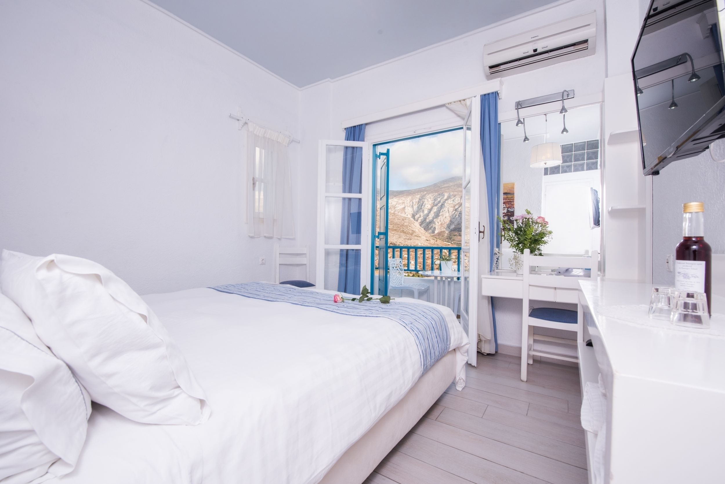 A bedroom with a bed, a desk, and a view of a mountainous landscape through an open window.
