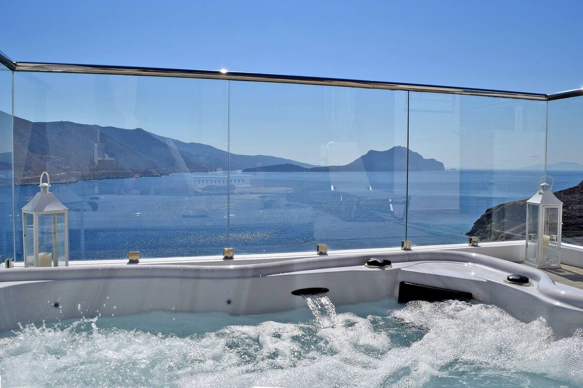 A glass-enclosed hot tub with a view of the sea and mountains.