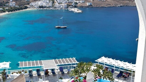 Tavolo apparecchiato per due con vista su una cittadina costiera e mare azzurro.