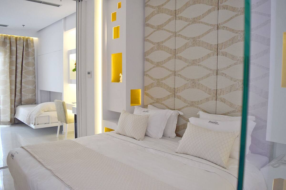 A modern hotel room with a large bed, a bedside table, a chair, and a patterned wall.
