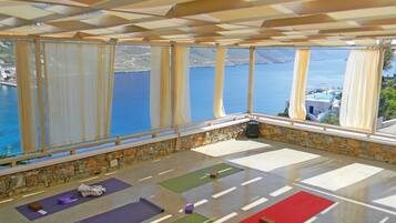 Una habitación con ventanas amplias que dan a una masa de agua, colchonetas de yoga y una pared de piedra.