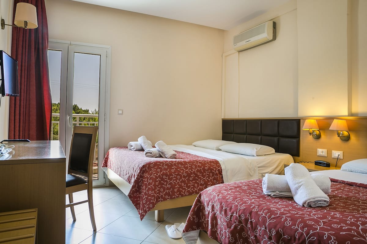 Habitación de hotel con dos camas, un escritorio, una silla y un balcón.