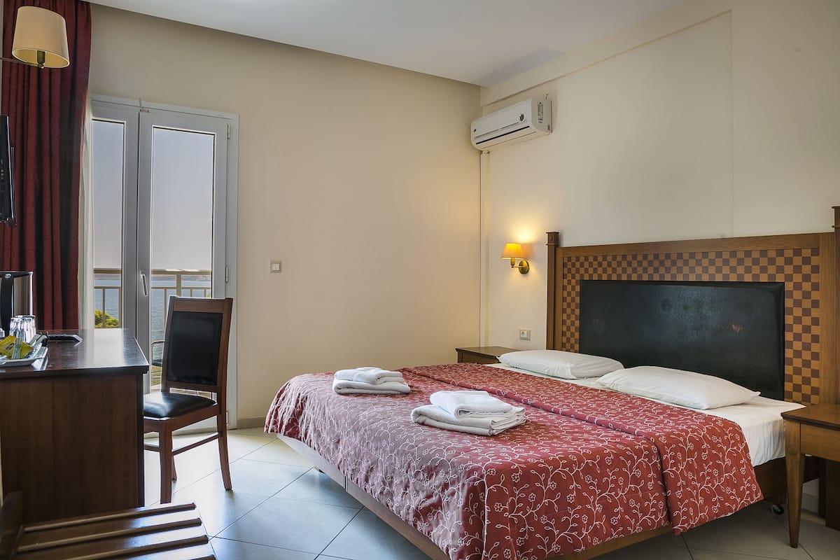 Habitación de hotel con cama, escritorio, silla, aire acondicionado y ventana con cortinas.