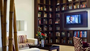 Ein modernes Wohnzimmer mit einer Couch, einem Couchtisch, einem gemusterten Sessel, einem großen Bücherregal, einem Fernseher und einer dekorativen Bambuspflanze.