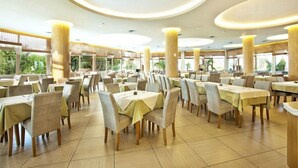 Un comedor espacioso con varias mesas y sillas, ventanas amplias y un diseño de techo moderno.