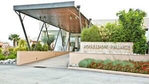La entrada al Palacio Poseidón, con un diseño arquitectónico moderno, un cartel y un área de jardín ajardinado.