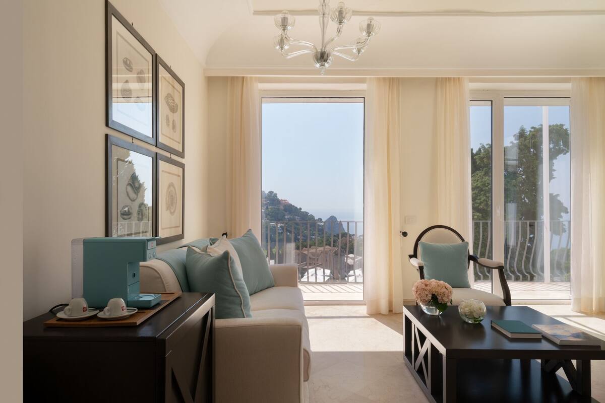 A living room with a sofa, a coffee table, and a view of a balcony with outdoor furniture.