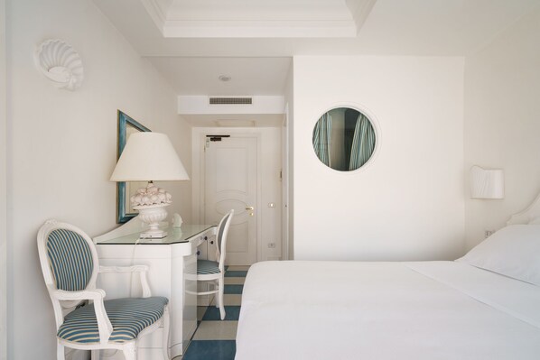 Una habitación de hotel con una cama, un escritorio con una silla, una lámpara y un espejo redondo en la pared.