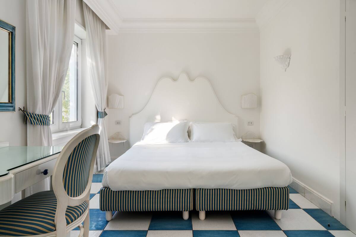 A bedroom with a large bed, a desk with a chair, and a window with curtains.
