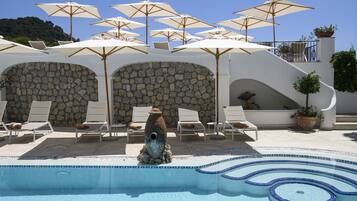 A pool area with lounge chairs, umbrellas, and a stone wall.