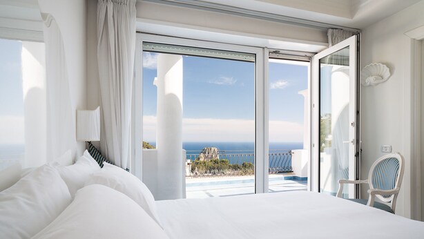 A bedroom with a large bed, a chair, and a balcony with a view of the sea. - La Residenza Capri (Capri)