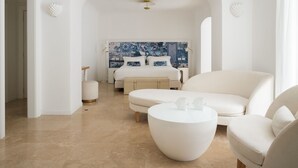 A modern bedroom with a large bed, a white sofa, a round coffee table, and a decorative headboard. - La Residenza Capri (Capri)