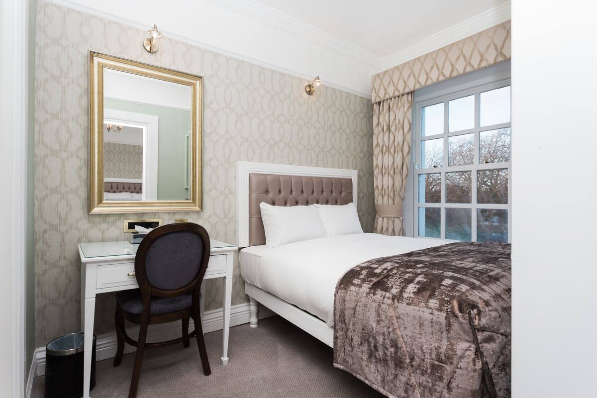 A hotel room with a bed, a desk, a chair, a mirror, and a window.