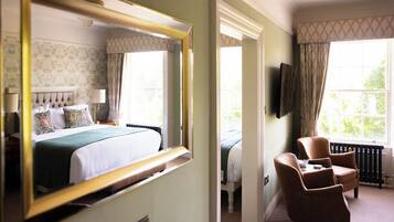 A hotel room with a large bed, a sitting area with a chair, a television mounted on the wall, and a window with curtains.