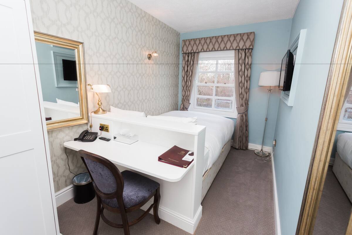 A hotel room with a bed, a desk with a chair, a telephone, a lamp, and a television.