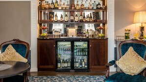 Zona de bar con estantes de botellas de licor, un refrigerador lleno de botellas y dos sillones con cojines decorativos.
