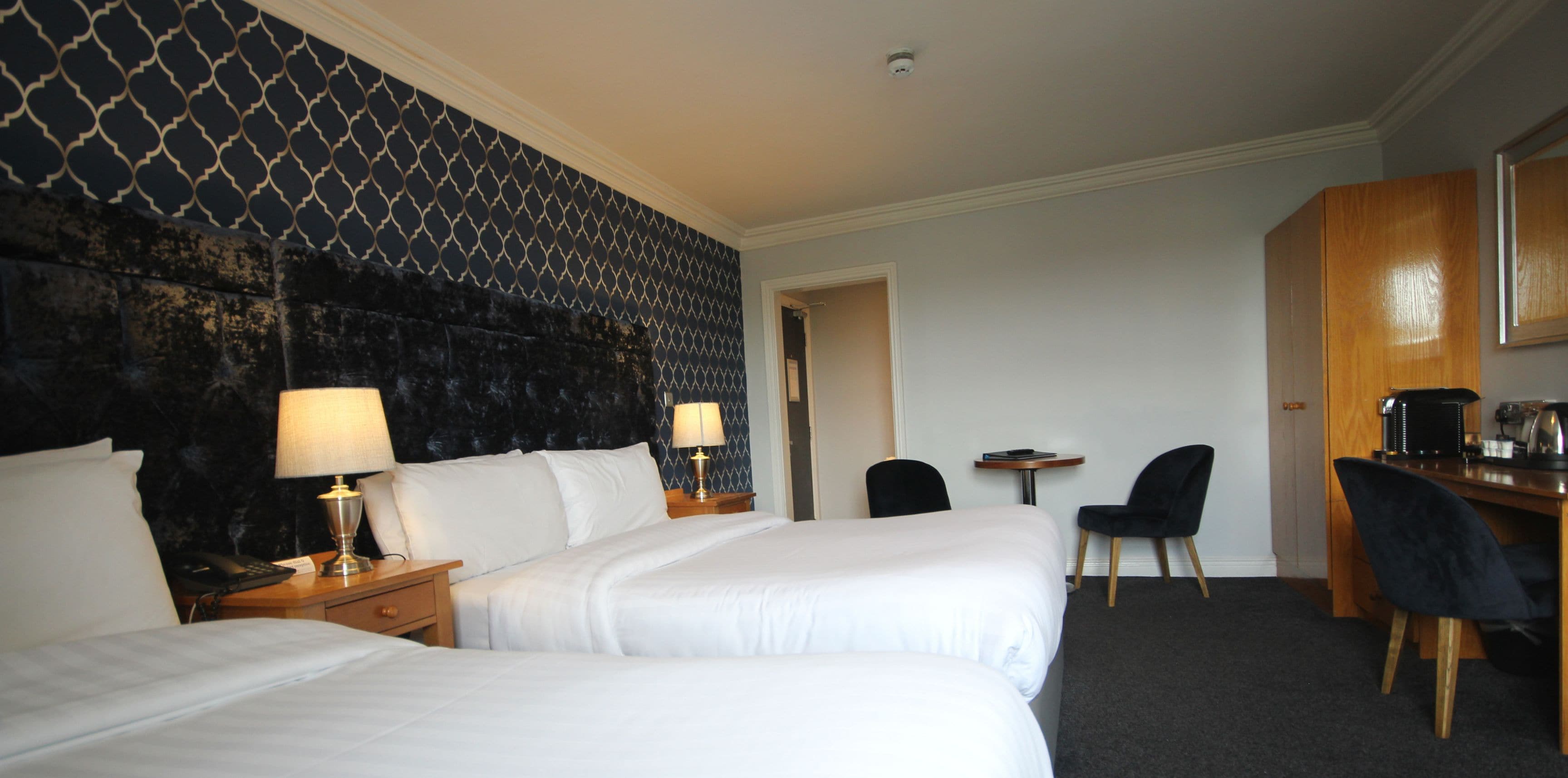 Een hotelkamer met twee bedden, een bureau, een stoel, een kleine tafel en een koffiezetapparaat.