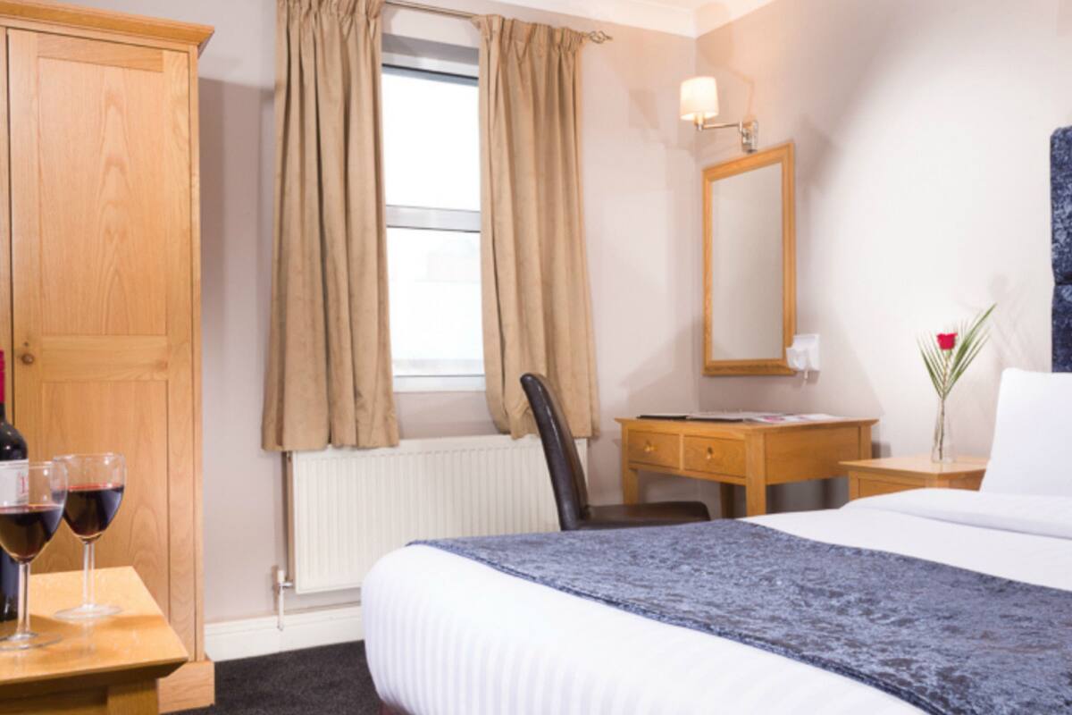 A hotel room with a bed, a desk, a chair, a wardrobe, and a window with curtains.