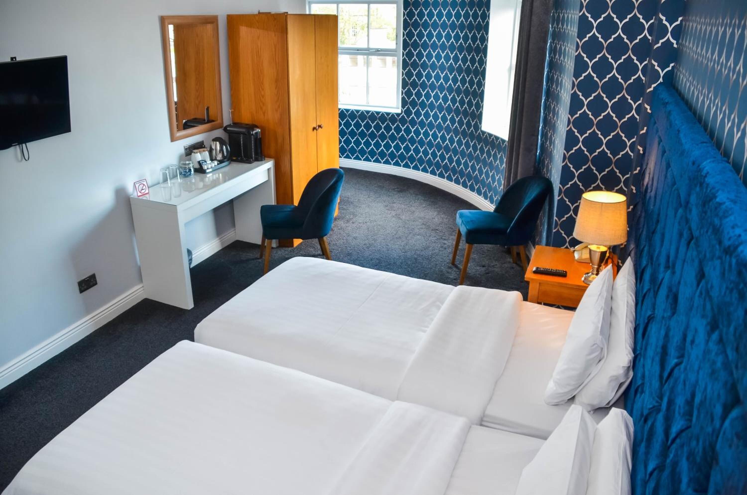 Une chambre d’hôtel avec deux lits, un bureau avec une chaise, une télévision et une fenêtre donnant sur un paysage agréable.