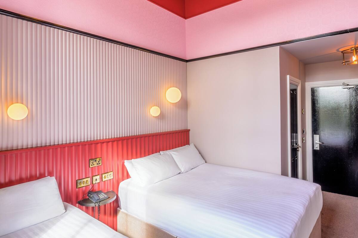 A hotel room with two beds, a red accent wall, a ceiling light fixture, and a door.