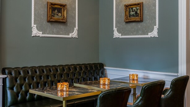 A dining area with a black leather sofa, a marble-top table, and four black chairs. There are two wall-mounted light fixtures above the sofa, and two framed pictures on the wall. - Hotel St. George by Nina (Dublin)