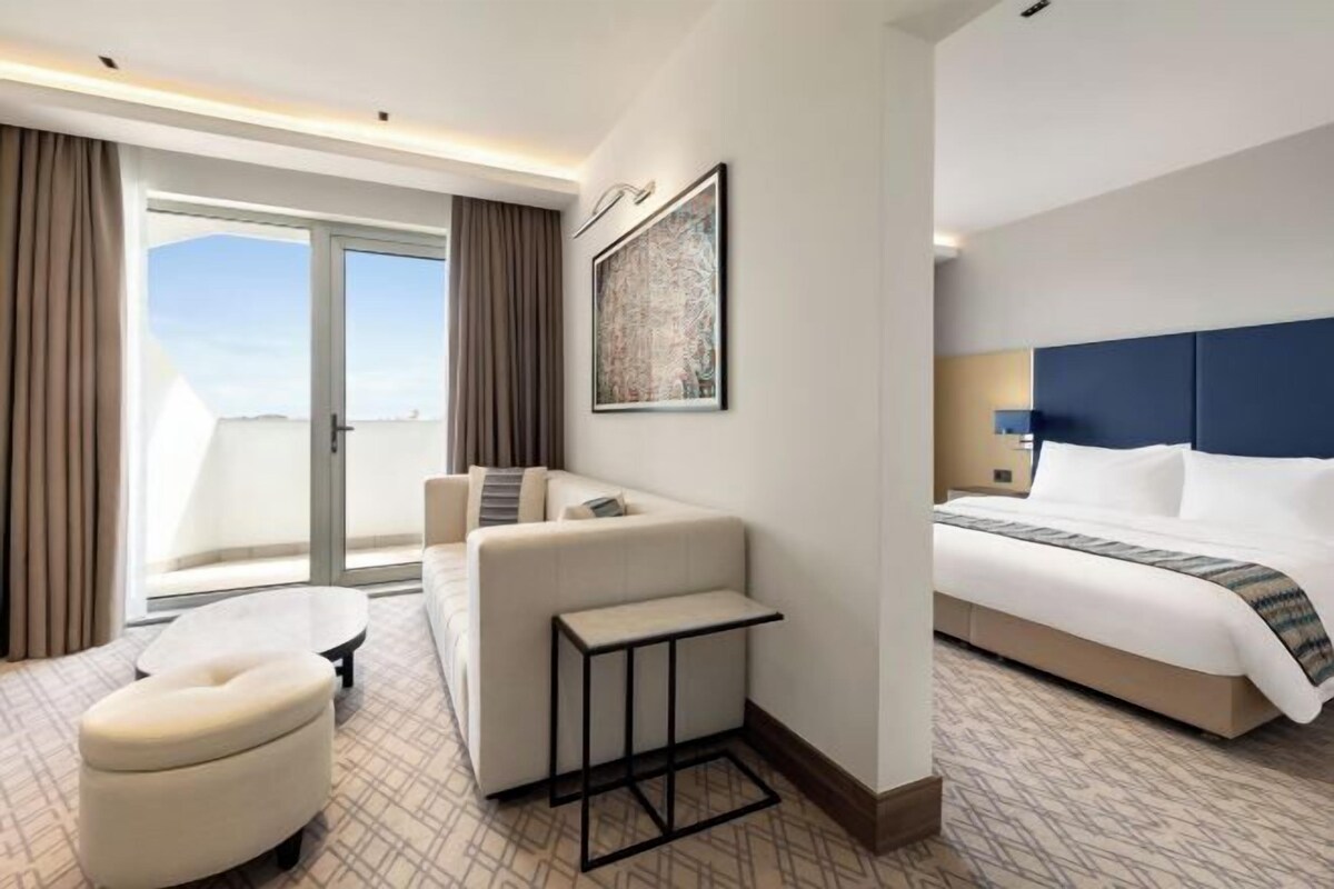 Habitación de hotel con cama, sofá, una mesita y vista al exterior.