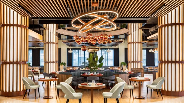 A modern dining area with round tables, chairs, and a central decorative light fixture. - Wyndham Bukhara (Bukhara)