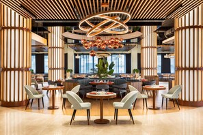 A modern dining area with round tables, chairs, and a central decorative light fixture. - Wyndham Bukhara (Bukhara)